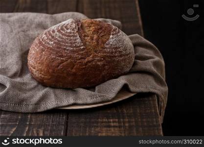 Freshly baked bread with kitchen towel on dark wooden board