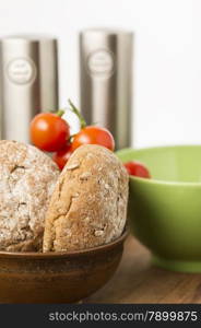 Freshly baked brown wholegrain bread rolls. Freshly baked brown wholegrain bread rolls in a bowl in the kitchen with a bunch of cherry tomatoes ready to prepare a healthy sandwich snack