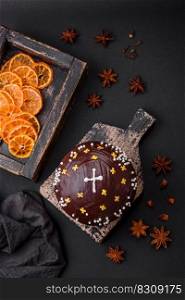 Freshly baked Easter cake or panettone with chocolate coating and raisins inside on a wooden cutting board on a dark concrete background