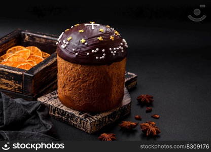 Freshly baked Easter cake or panettone with chocolate coating and raisins inside on a wooden cutting board on a dark concrete background