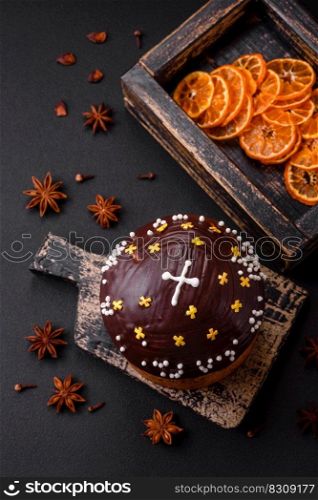 Freshly baked Easter cake or panettone with chocolate coating and raisins inside on a wooden cutting board on a dark concrete background
