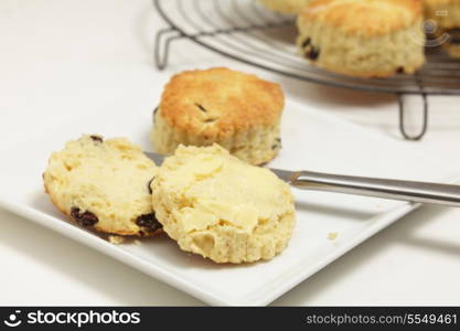 "Freshly-baked fruit scones, with one on a plate cut open and buttered. Scones - similar to American "biscuits" are a traditional British tea-cake."