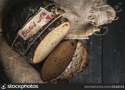 Freshly baked healthy brown bread and baked with heart etiquette, on a jute sack, on a rustic kitchen table. Above view of sliced German rye bread.