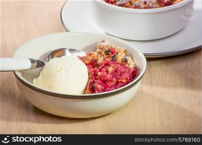 Freshly baked mixed berry crumble in a small dish, served with vanilla ice cream.