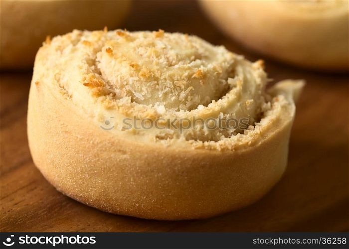 Freshly baked sweet coconut roll on wooden plate, photographed with natural light (Selective Focus, Focus on the front of the middle part of the roll)