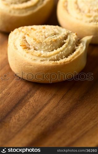 Freshly baked sweet coconut rolls on wooden plate, photographed with natural light (Selective Focus, Focus in the middle of the first roll)