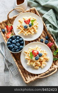 Freshly baked waffles with strawberries and blueberries on a concrete gray background.  Homemade baking.