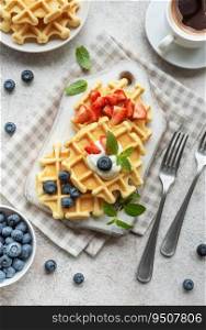 Freshly baked waffles with strawberries and blueberries on a concrete gray background.  Homemade baking.