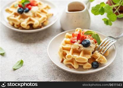 Freshly baked waffles with strawberries and blueberries on a concrete gray background.  Homemade baking.