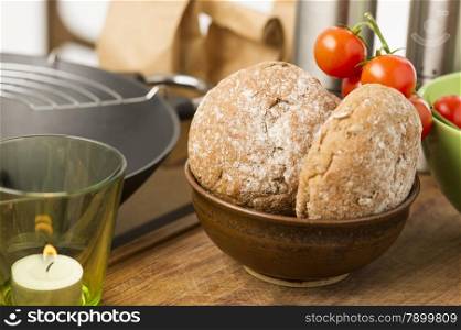 Freshly baked wholegrain brown rolls. Freshly baked wholegrain brown rolls with a burning candle on a kitchen counter with cherry tomatoes for preparing a salad