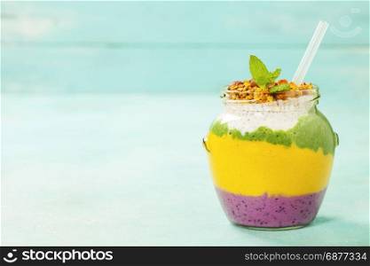 Freshly blended fruit smoothie in glass jar with straw. Turquoise blue background, copy space