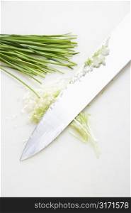 Freshly chopped chives with kitchen knife resting on countertop.
