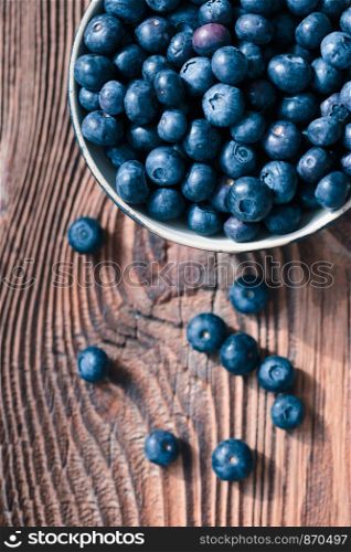 Freshly gathered blueberries put into ceramic bowl. Some fruits freely scattered on old wooden table. Shot from above