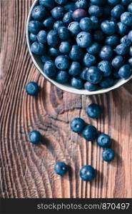 Freshly gathered blueberries put into ceramic bowl. Some fruits freely scattered on old wooden table. Shot from above