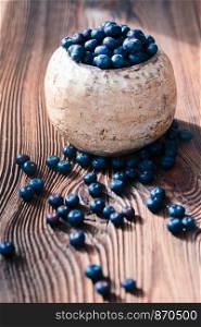 Freshly gathered blueberries put into old ceramic bowl. Some fruits freely scattered on old wooden table