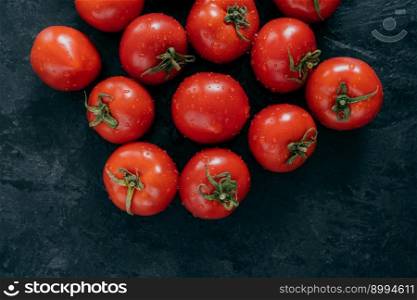 Freshly harvested red tomatoes with green leaves on dark background. Organic natural healthy food. Juicy raw tomatoes. Fresh vegetables