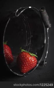 Freshly harvested strawberries in a black bucket, in low light. Picking strawberries concept. Tasty fresh strawberry close-up on black background.