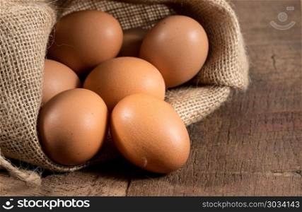 Freshly laid organic eggs in burlap sack on wood. Easter background with brown organic eggs arranged inside a burlap sack on rustic wooden table. Freshly laid organic eggs in burlap sack on wood