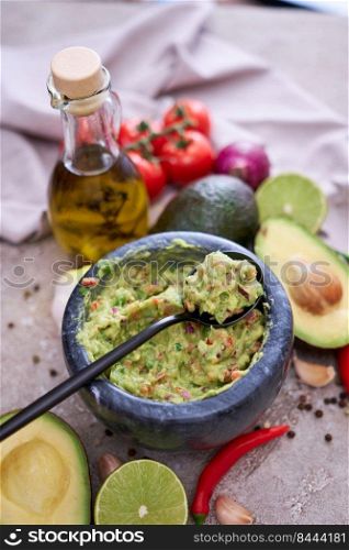 freshly made guacamole in marble mortar with ingredients on grey concrete background.. freshly made guacamole in marble mortar with ingredients on grey concrete background