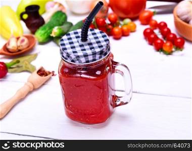 Freshly made juice from a ripe red tomato in a glass jar with a straw on a white wooden background