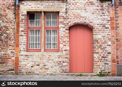 Freshly painted door on old European stone house of Bruges, Belgium in a color of the year 2019 Living Coral Pantone.. Facade brick old wall with painted door in a trendy color of the year 2019 Living Coral Pantone.