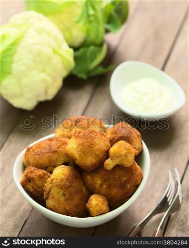 Freshly prepared breaded cauliflower in bowl with mayonnaise to dip and raw cauliflower in the back (Selective Focus, Focus on the front of the top cauliflower heads in the bowl)