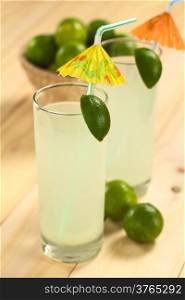 Freshly prepared refreshing lemonade out of limes in tall glass garnished with lime wedge and paper parasol (Selective Focus, Focus on the lime wedge)