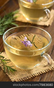 Freshly prepared rosemary herbal tea in glass cups, garnished with rosemary flowers, photographed on dark wood with natural light (Selective Focus, Focus on the first flowers)