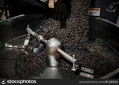 Freshly roasted coffee beans pouring from a large coffee roaster into the cooling cylinder. 