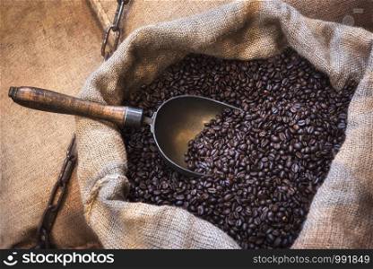 Freshly roasted coffee beans with a metal scoop, in jute sacks. Close-up with an open coffee bag. Coffee shop context. Arabic coffee beans in bag.