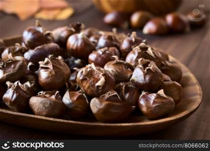Freshly roasted or baked chestnuts on wooden plate, photographed with natural light (Selective Focus, Focus one third into the image)