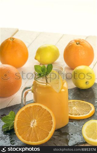Freshly squeezed orange juice in a jar, surrounded by oranges and lemons slices in a warm summer light