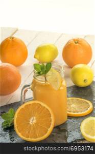 Freshly squeezed orange juice in a jar, surrounded by oranges and lemons slices in a warm summer light