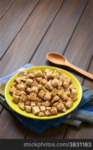 Freshly toasted homemade croutons made of wholegrain bread, photographed on dark wood with natural light (Selective Focus, Focus one third into the croutons)