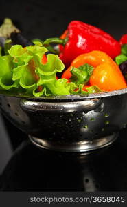 Freshly washed fresh vegetables in a metal colander isolated over black background.