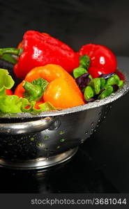 Freshly washed fresh vegetables in a metal colander isolated over black background.