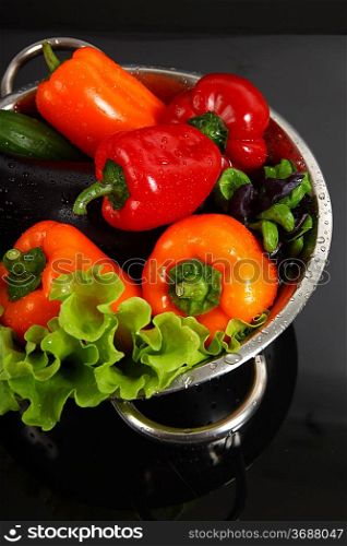 Freshly washed fresh vegetables in a metal colander isolated over black background.