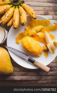 freshness fruit mango lying on a white plate with knife. Fresh shake with milk and straw on brown board rustic