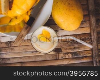 freshness fruit mango lying on a white plate with knife. Fresh shake with shape heart love mango slices milk and straw on brown board rustic