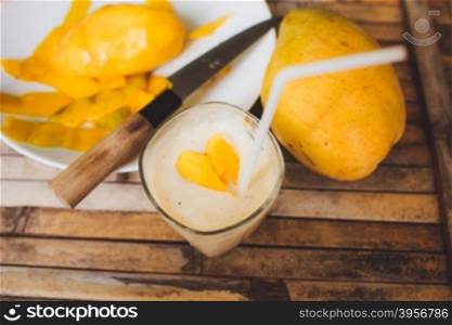 freshness fruit mango lying on a white plate with knife. Fresh shake with shape heart love mango slices milk and straw on brown board rustic