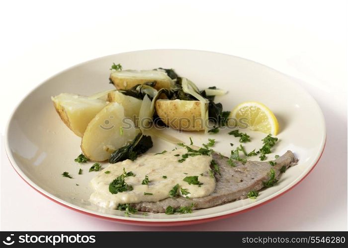 Fried and peppered escalope of veal served with potatoes mixed with wilted chard and a creamy gravy, all garnished with chopped herbs and served with a lemon wedge, from above