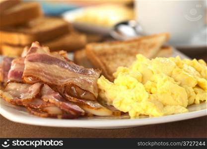 Fried bacon and scrambled eggs wth toast bread in the back (Selective Focus, Focus on the lower edge of the bacon on top) . Bacon and Egg