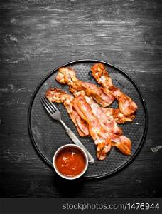 Fried bacon and tomato sauce. On a black wooden background.. Fried bacon and tomato sauce. On black wooden background.