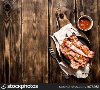 Fried bacon in a frying pan and tomato sauce. On a wooden table.. Fried bacon in a frying pan and tomato sauce.