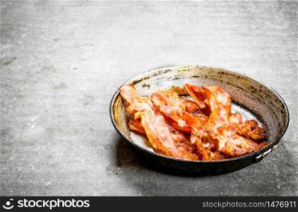 Fried bacon in a frying pan. On a stone background.. Fried bacon in a frying pan. On stone background.