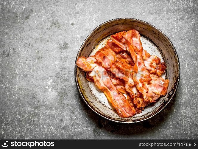 Fried bacon in a frying pan. On a stone background.. Fried bacon in a frying pan. On stone background.