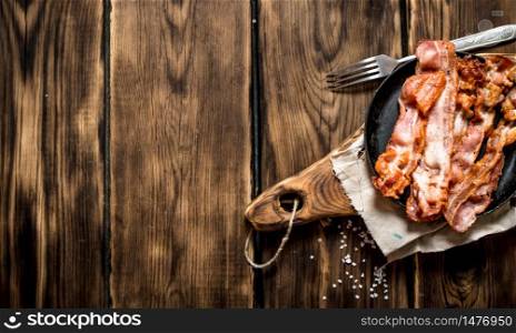 Fried bacon in a frying pan with a fork. On a wooden table.. Fried bacon in a frying pan