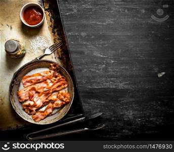 Fried bacon in a frying pan with the sauce. On a black wooden background.. Fried bacon in a frying pan with the sauce.