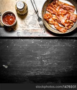 Fried bacon in a frying pan with the sauce. On a black wooden background.. Fried bacon in a frying pan with the sauce.