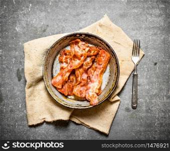 Fried bacon in a pan on the fabric. On a stone background.. Fried bacon in a pan on the fabric.
